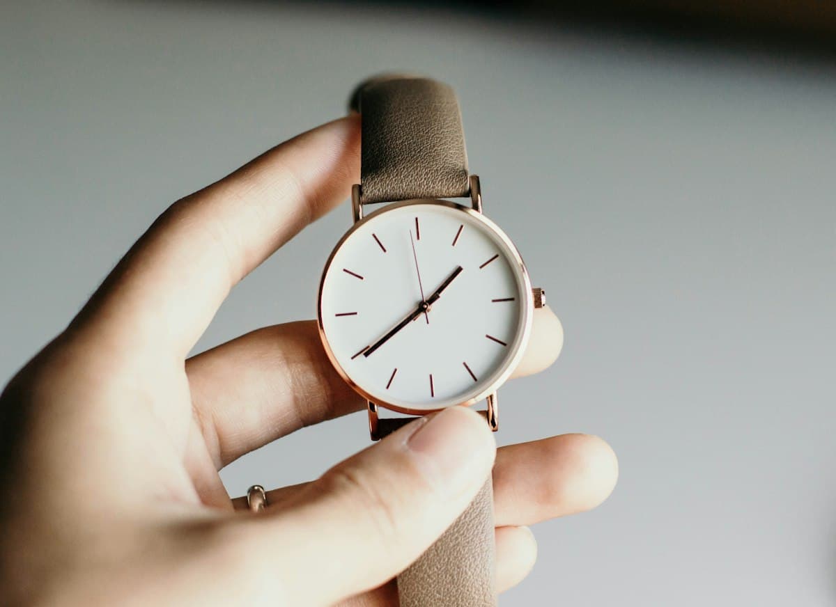Reloj analógico de carátula blanca sostenido en la mano