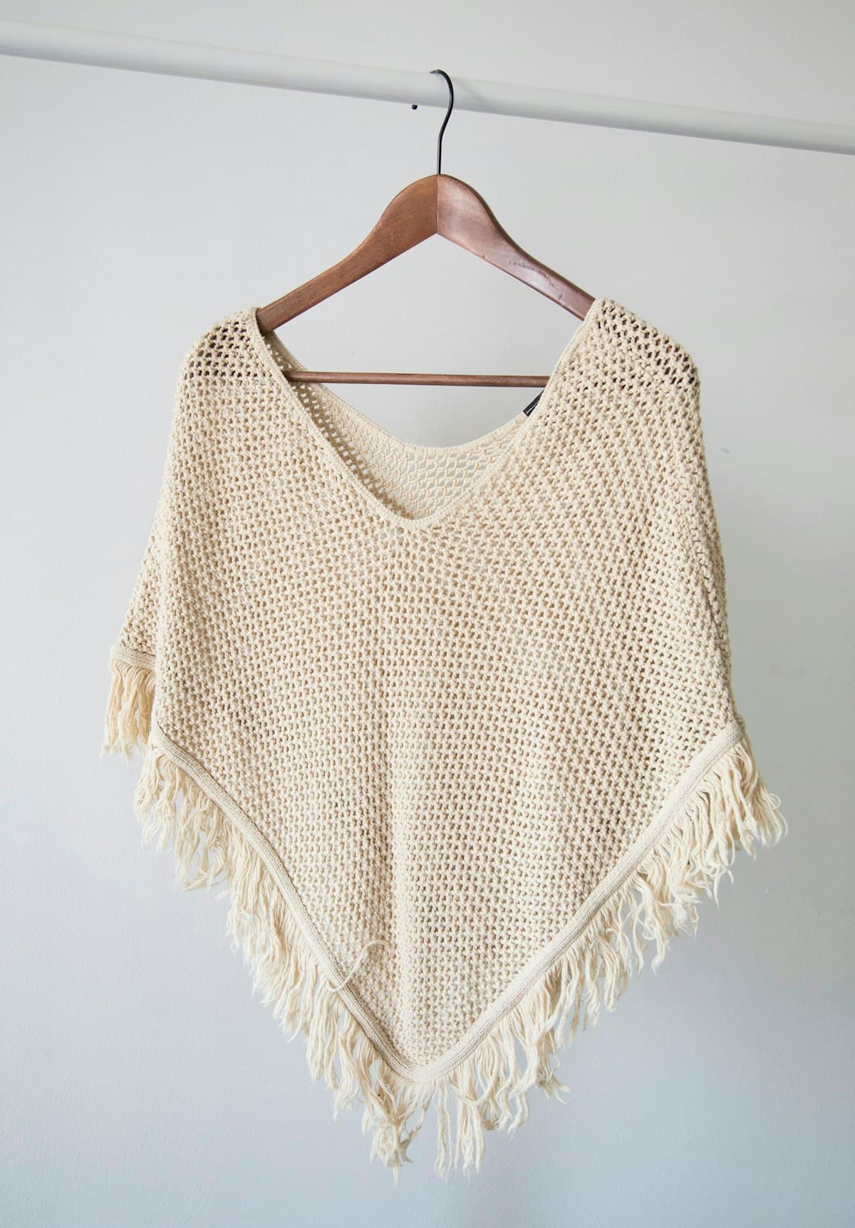 Poncho tejido color crudo colgado en un gancho